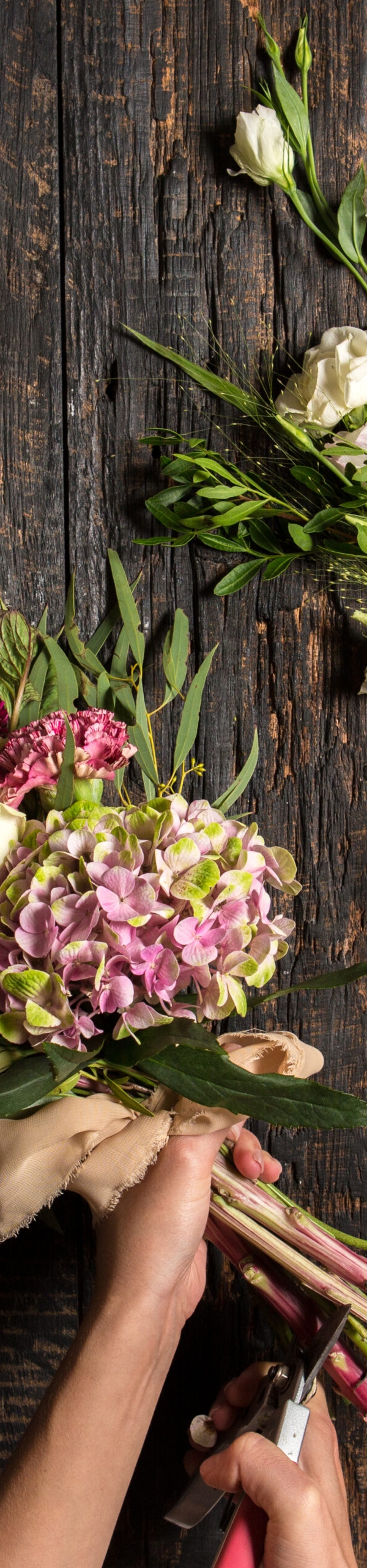 The hands of florist against desktop with working tools and ribbons on wooden background